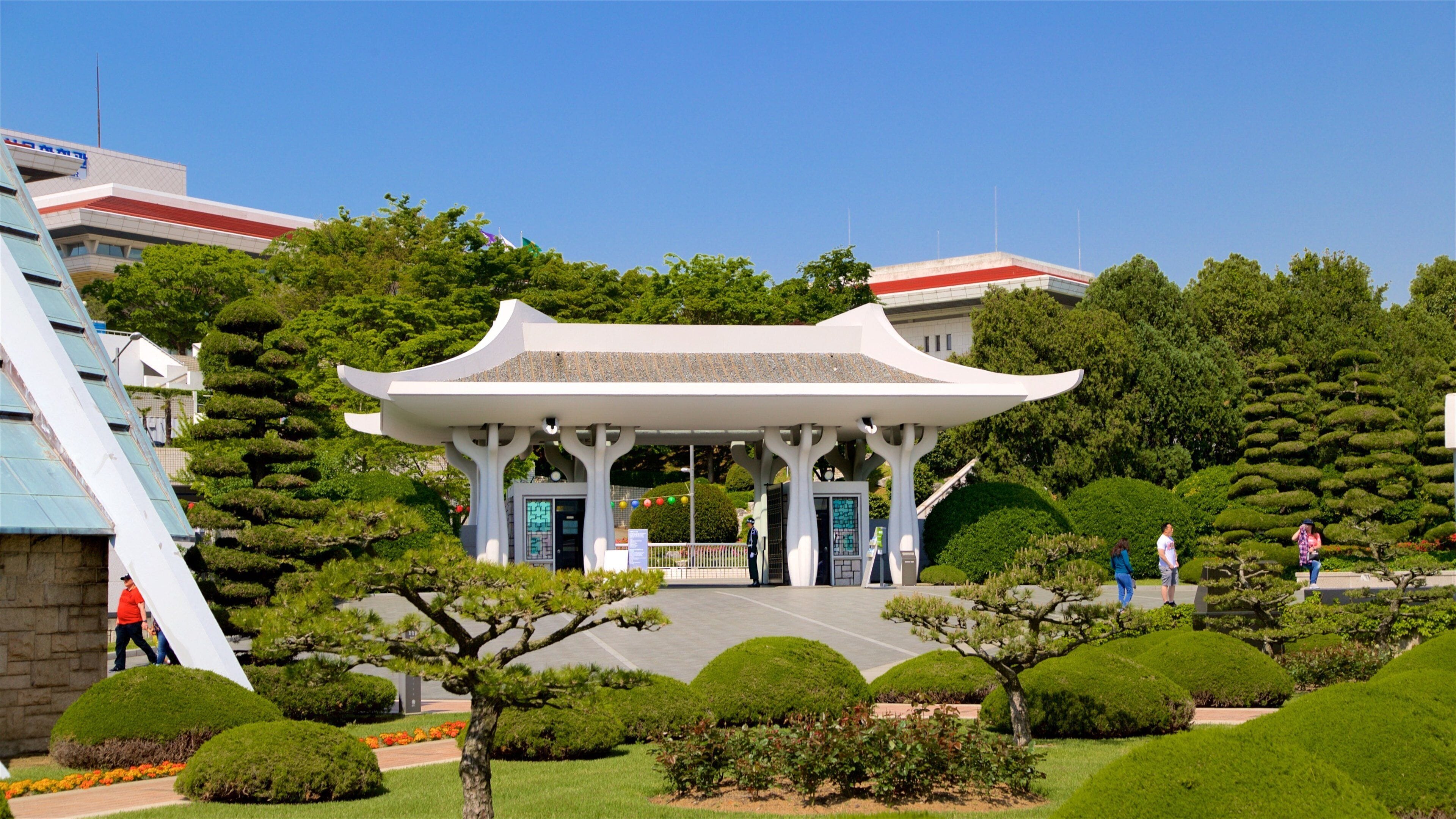 A traditional pavilion in a park with neatly trimmed trees and a clear blue sky.
