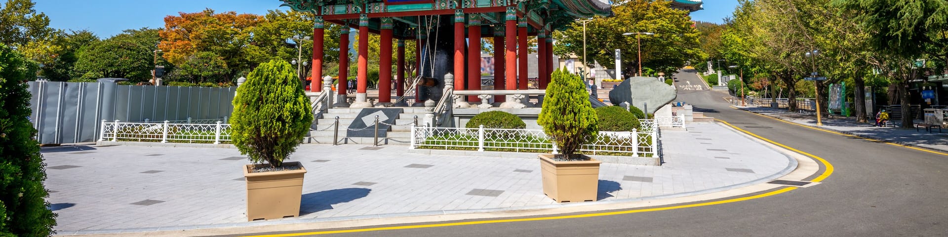 A traditional Korean pavilion with a tall white tower, surrounded by trees and a clear blue sky.