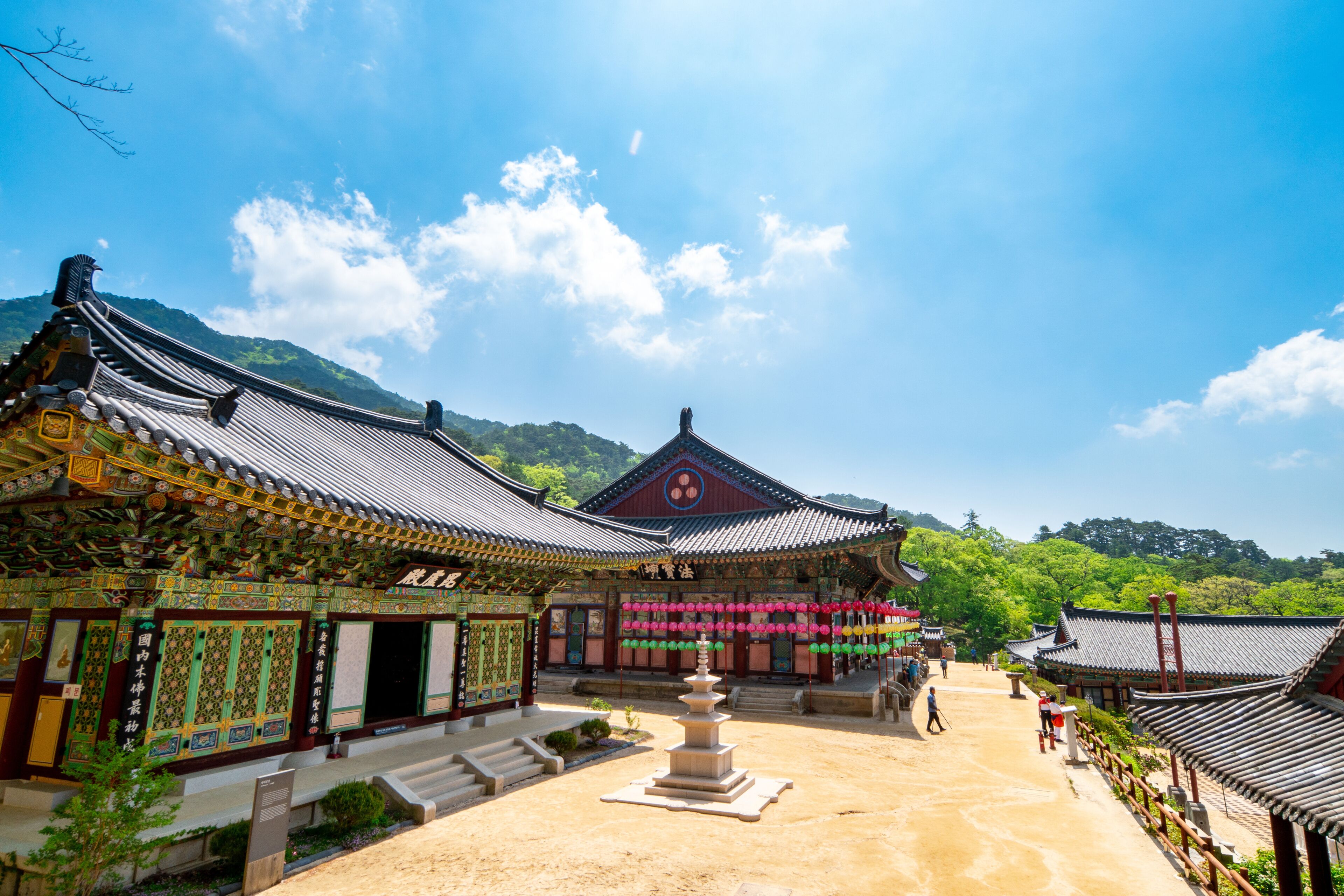 A traditional Korean temple complex with ornate architecture, a central stone pagoda, and a mountainous backdrop.