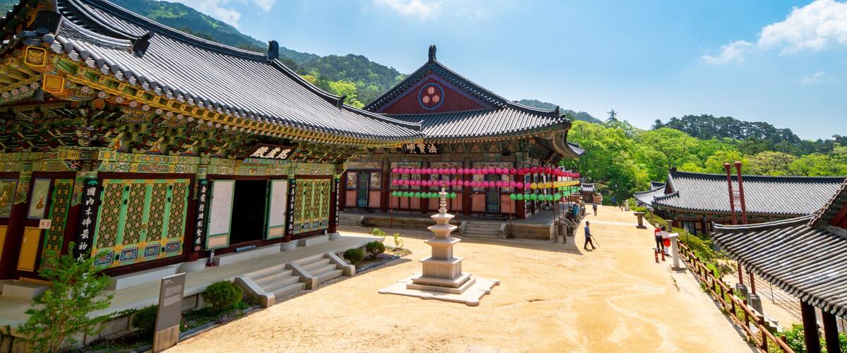 A traditional Korean temple complex with ornate architecture, a central stone pagoda, and a mountainous backdrop.