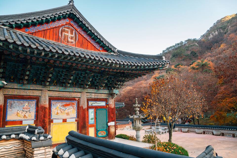 A traditional Korean temple with ornate architecture, a stone pagoda, and autumn foliage.