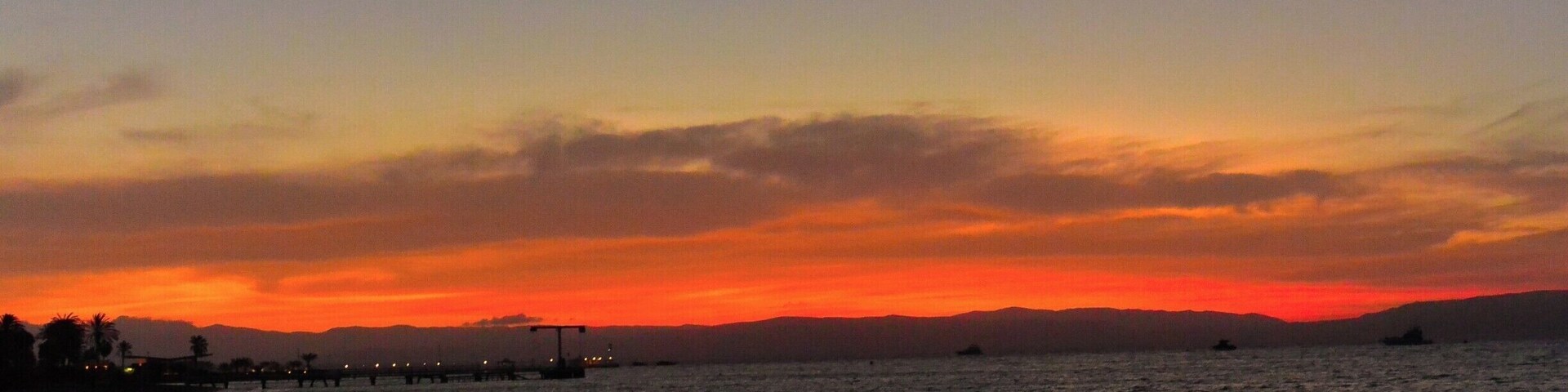 Una puesta de sol sobre una playa con un muelle que se adentra en el agua.