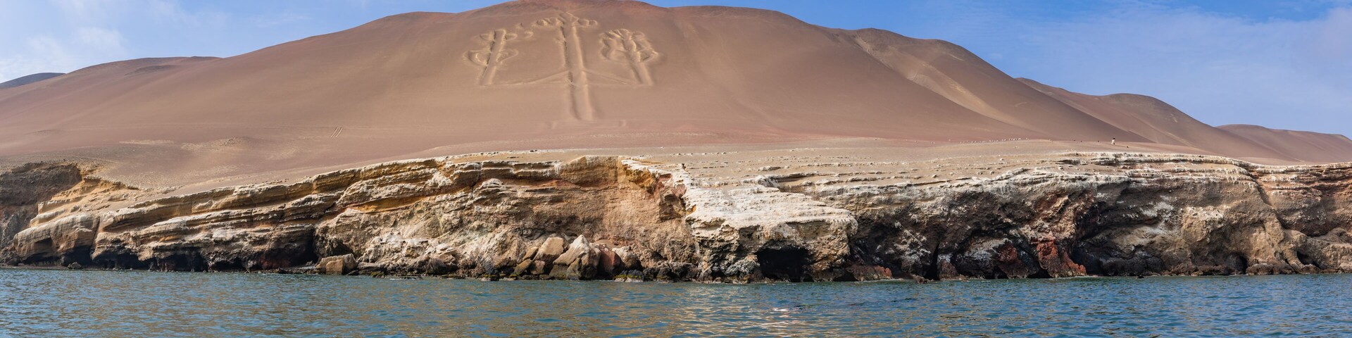 Paisagem desértica com uma duna de areia imensa e uma costa rochosa.