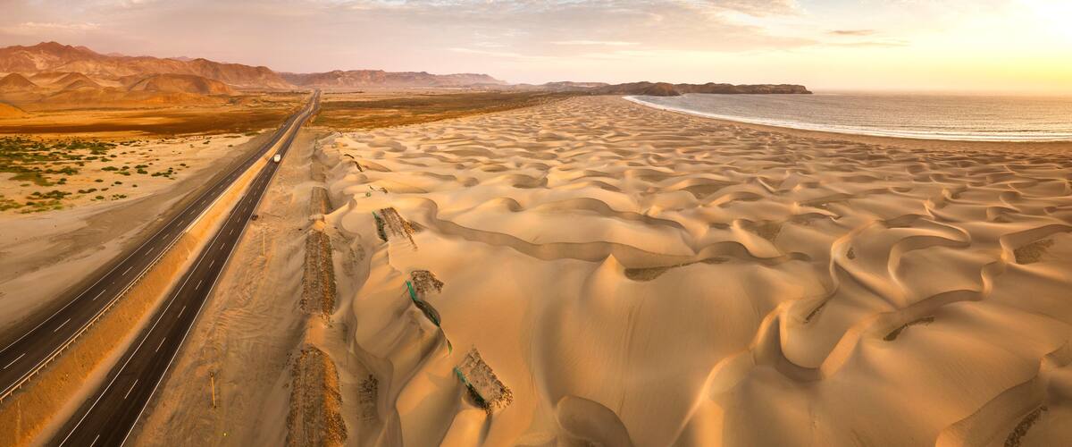 A desert landscape with a highway, sand dunes, and a coastline.