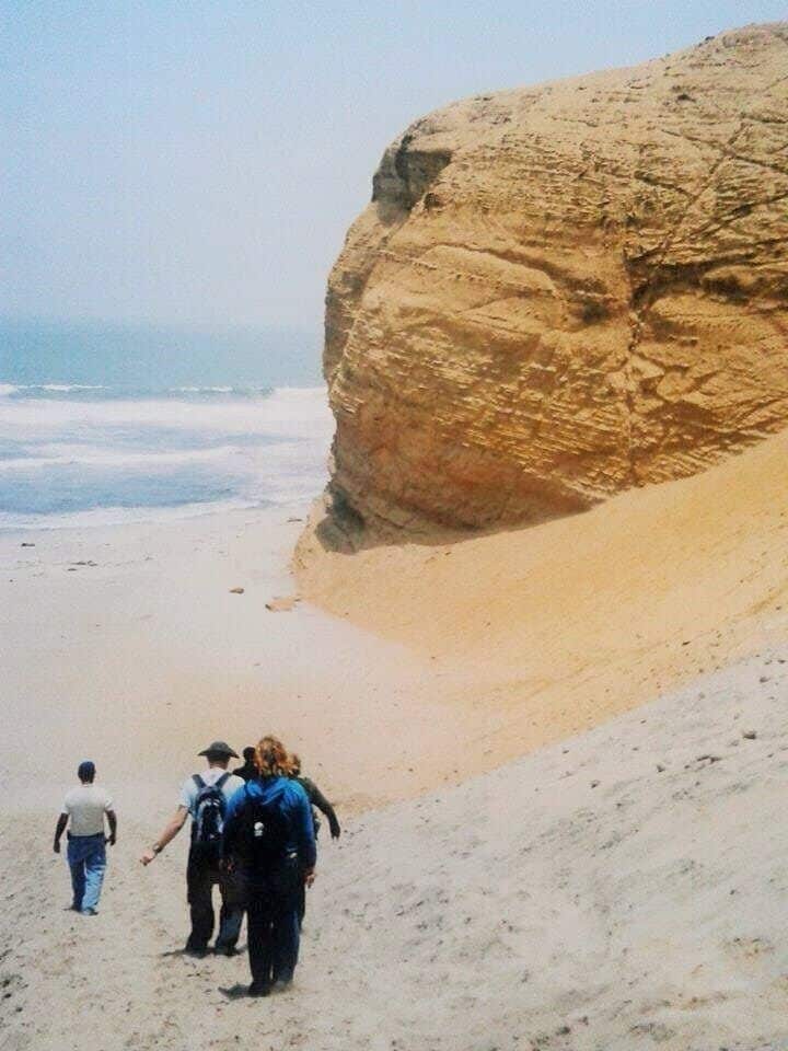 Una gran formación rocosa cerca de una playa, con gente caminando alrededor.