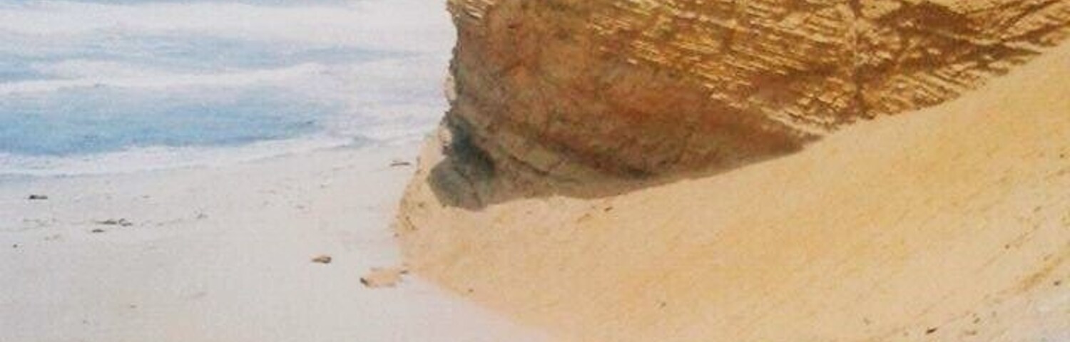 Una gran formación rocosa cerca de una playa, con gente caminando alrededor.