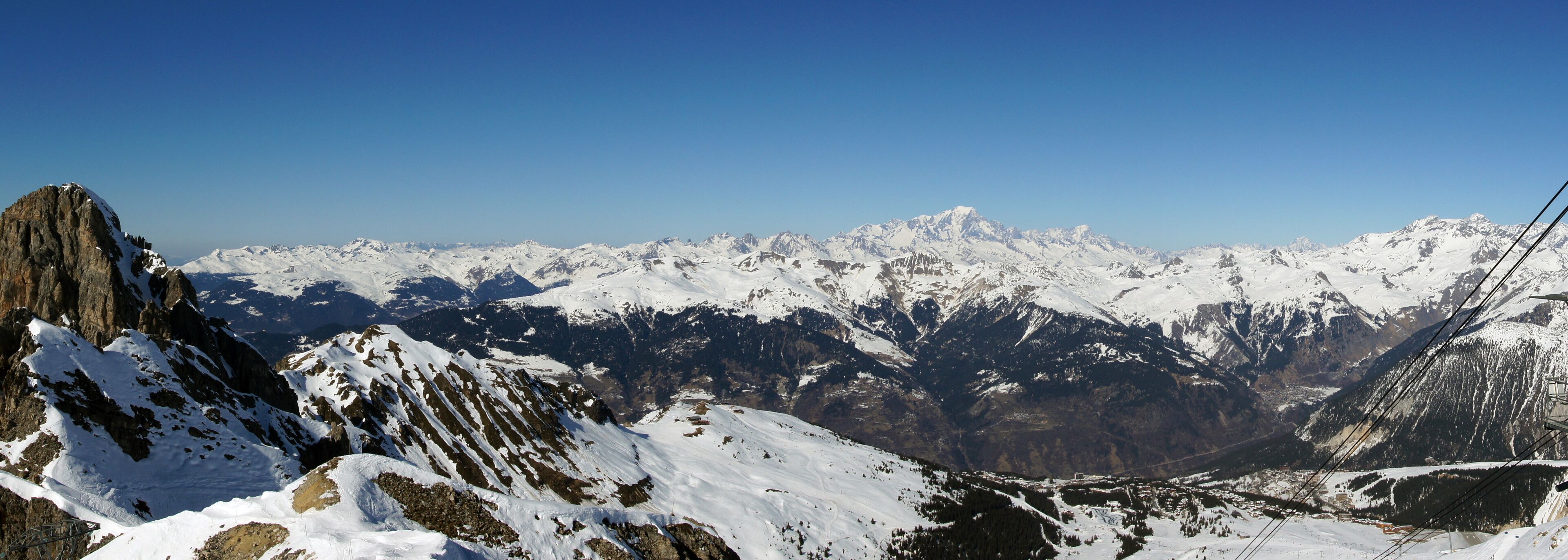 A snow-covered mountain range with rocky peaks and a clear blue sky.