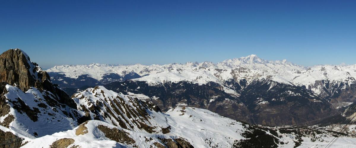 A snow-covered mountain range with rocky peaks and a clear blue sky.