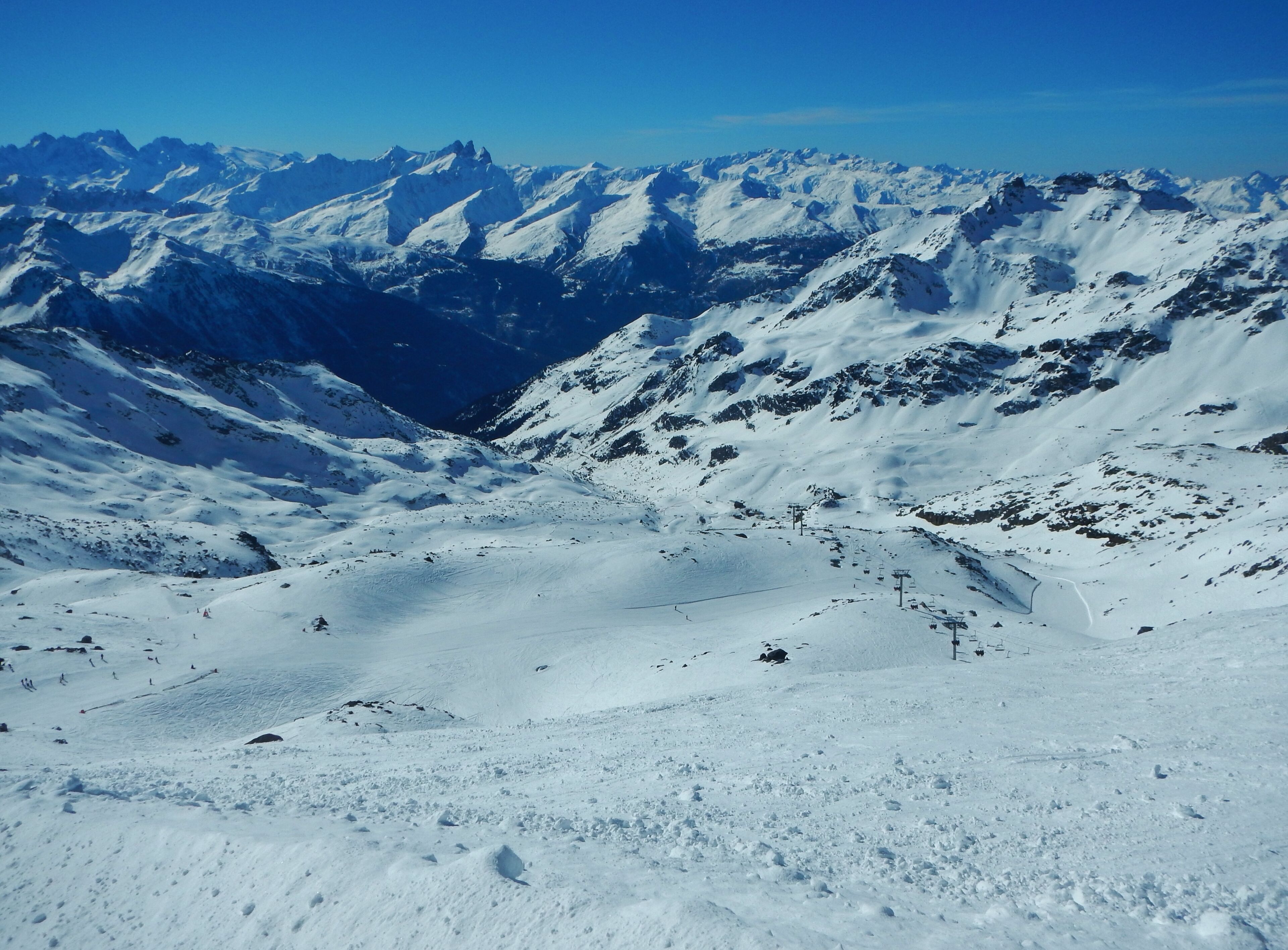 A snow-covered mountain range with ski slopes and a clear blue sky.