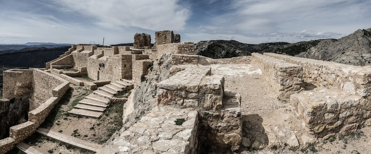 Ancient ruins with stone steps and walls, set against a mountainous backdrop.