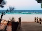 A wooden pier leading to a sandy beach with turquoise water and rocky outcrops.