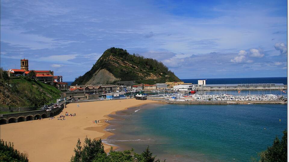 A coastal town with a sandy beach, a hill with a church, and a marina with boats.
