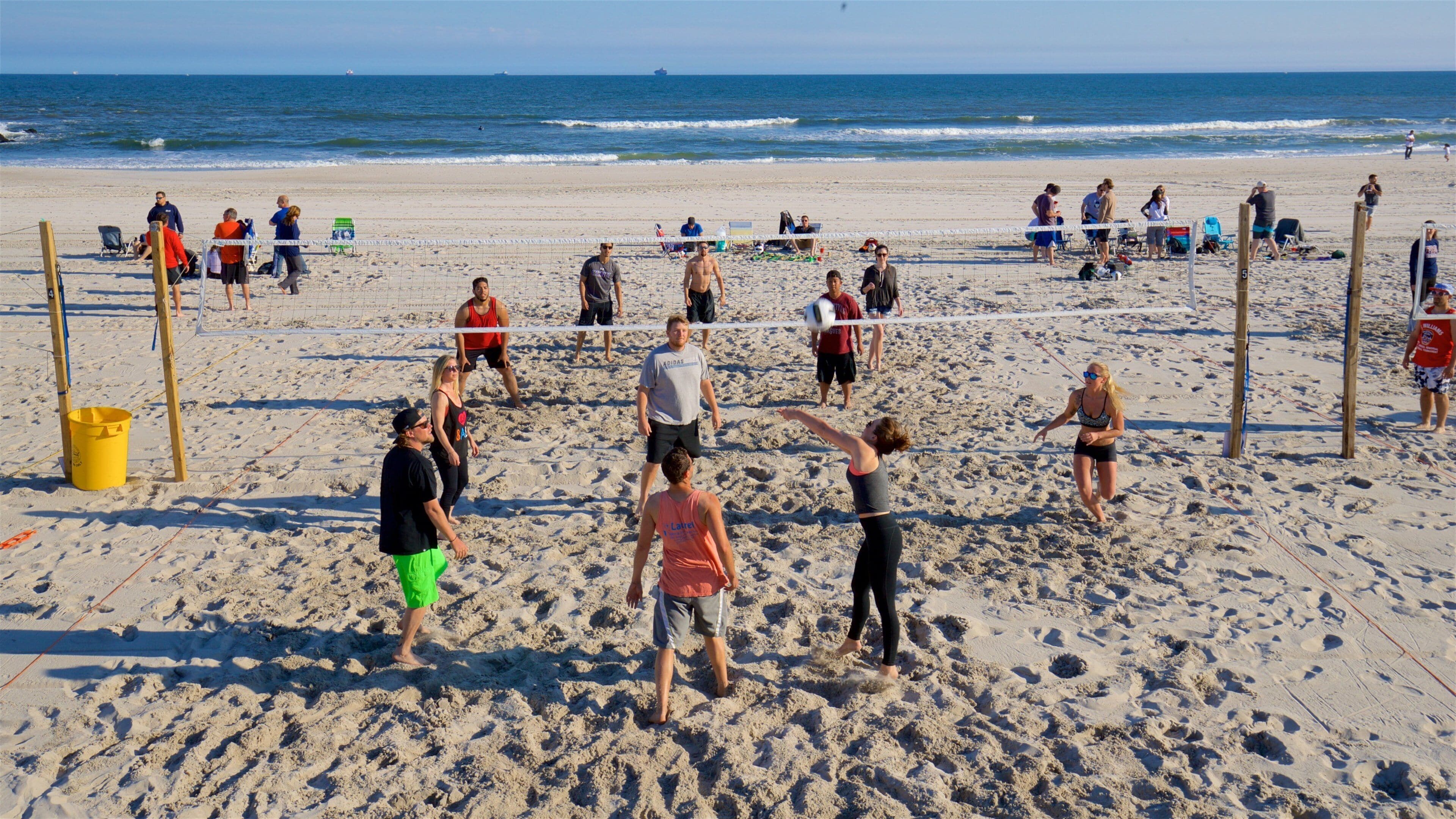 A beach volleyball game with players and spectators.