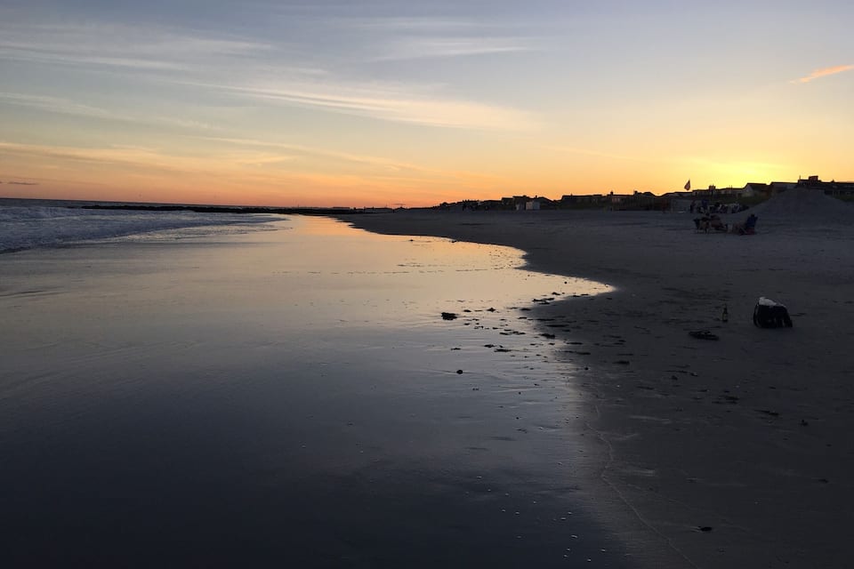 A beach at sunset with calm waters reflecting the sky.
