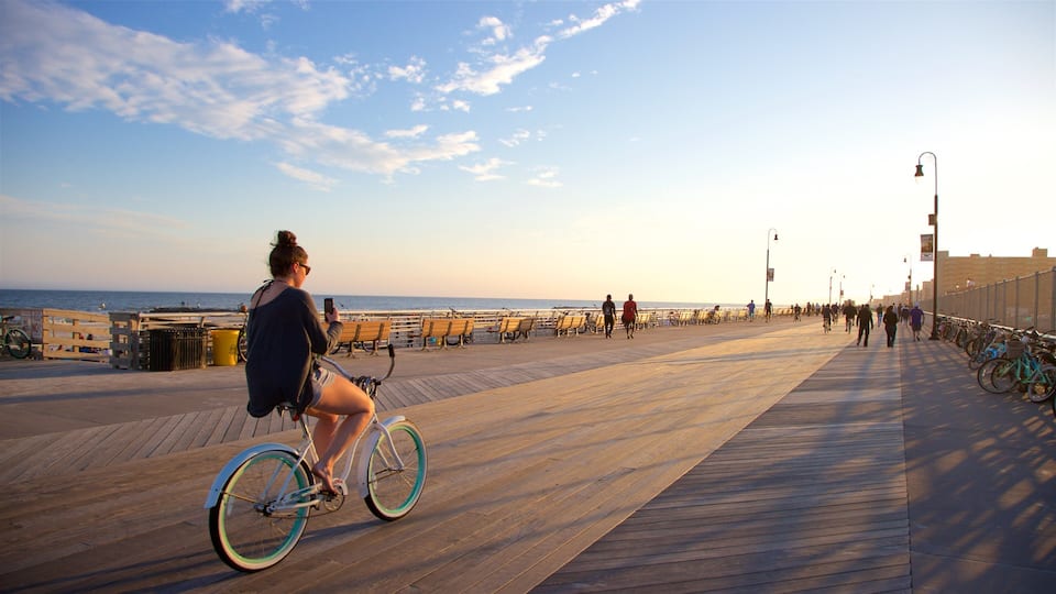 A wooden boardwalk by the ocean with benches and bicycles.
