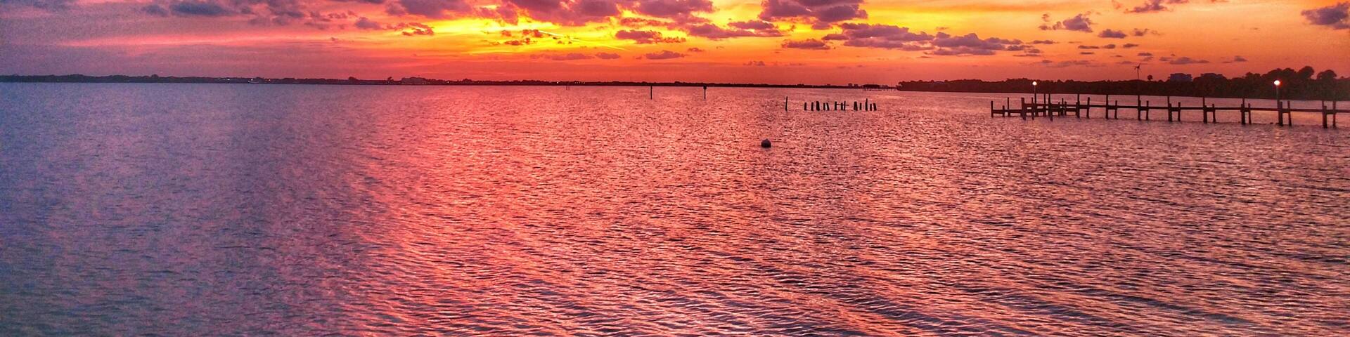 A sunset over a calm body of water with a wooden pier extending into the water.