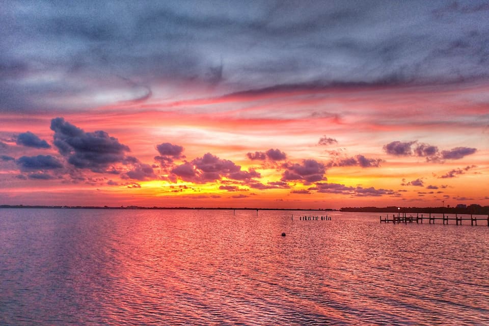Een zonsondergang boven een kalm wateroppervlak met een houten pier die het water in loopt.