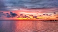 Een zonsondergang boven een kalm wateroppervlak met een houten pier die het water in loopt.