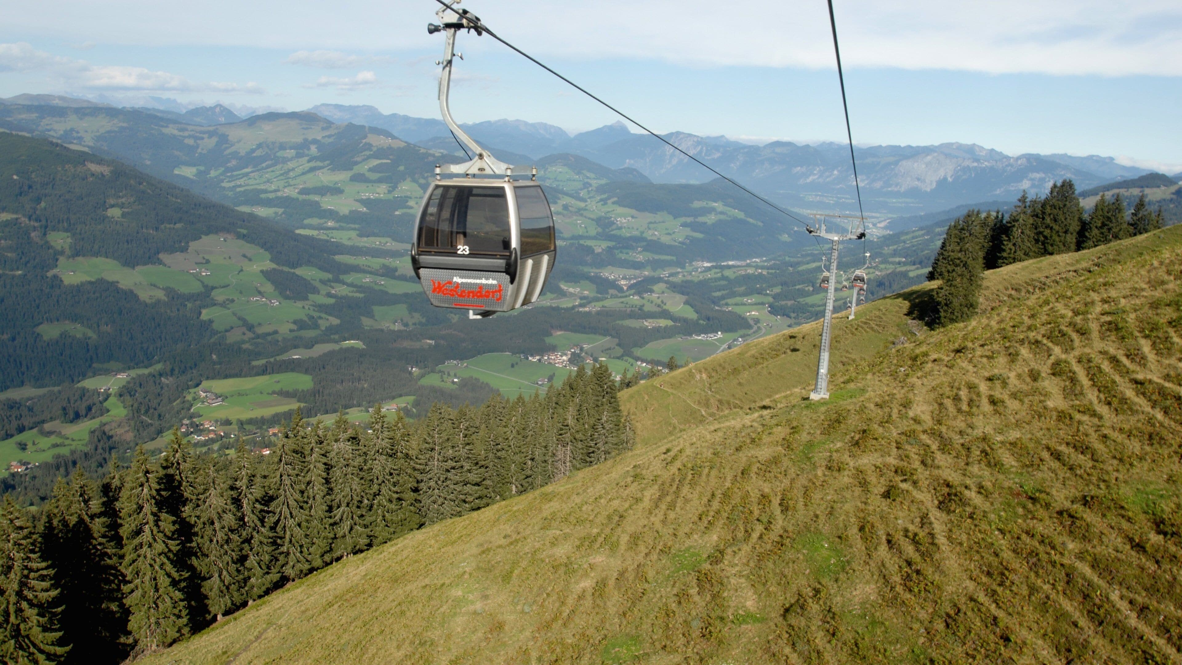 A cable car in a mountainous area with green valleys and forests.