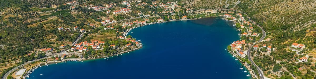 An aerial view of a coastal town with a bay, surrounded by hills and dotted with red-roofed buildings.