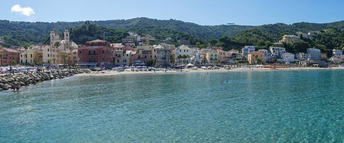 A coastal town with a clear blue sea, a beach with umbrellas, and a hill with a church in the background.