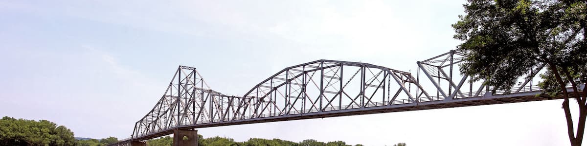 A steel truss bridge over a river with dense green foliage on both sides.