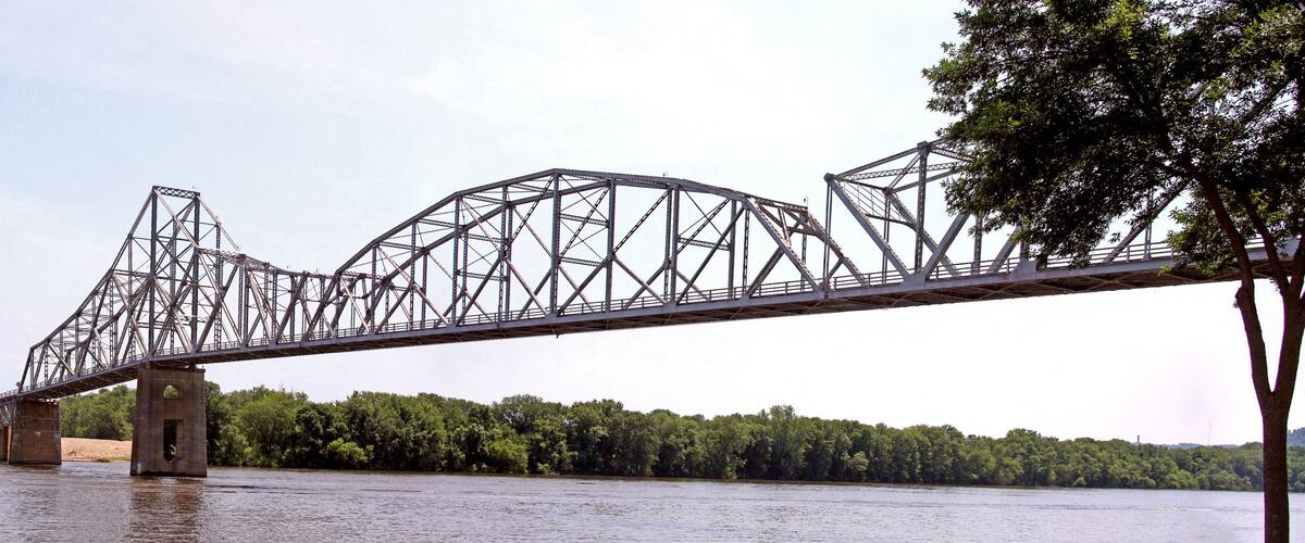 A steel truss bridge over a river with dense green foliage on both sides.