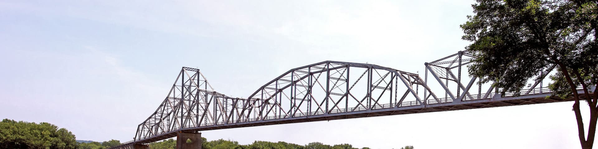 A steel truss bridge over a river with dense green foliage on both sides.