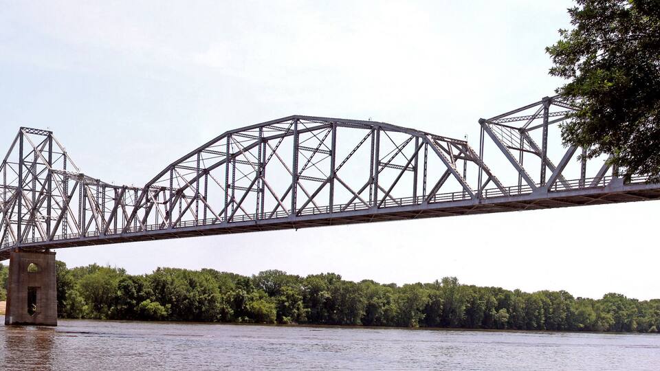 A steel truss bridge over a river with dense green foliage on both sides.