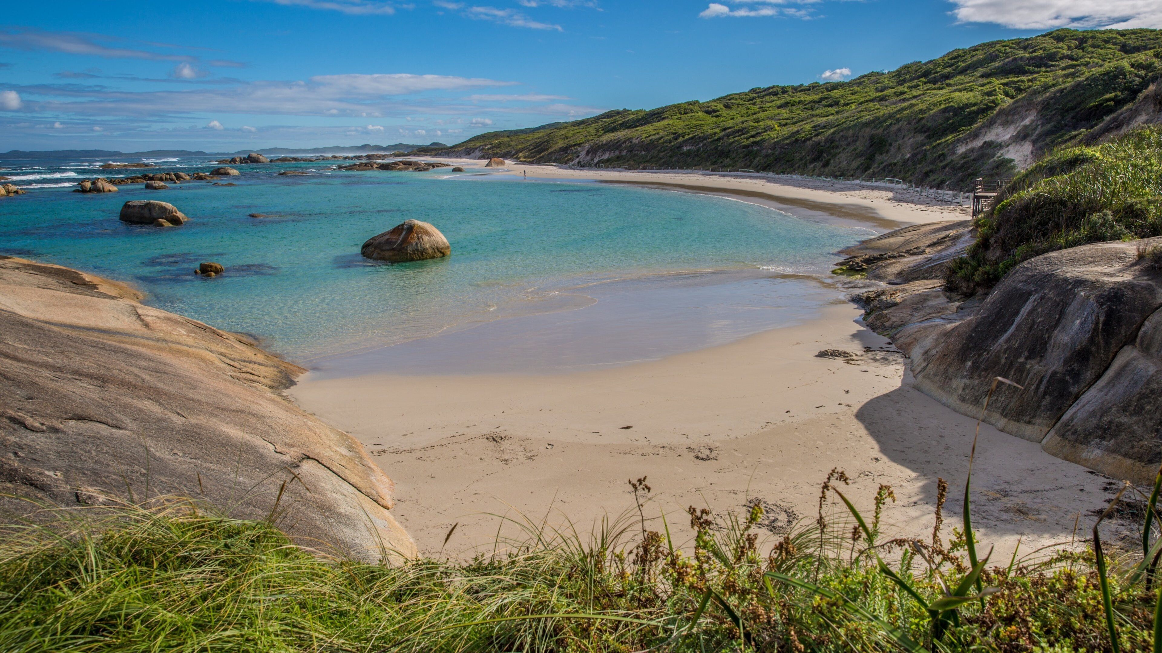 A coastal landscape with clear turquoise waters, sandy beach, and rocky outcrops.