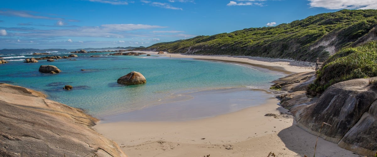 A coastal landscape with clear turquoise waters, sandy beach, and rocky outcrops.