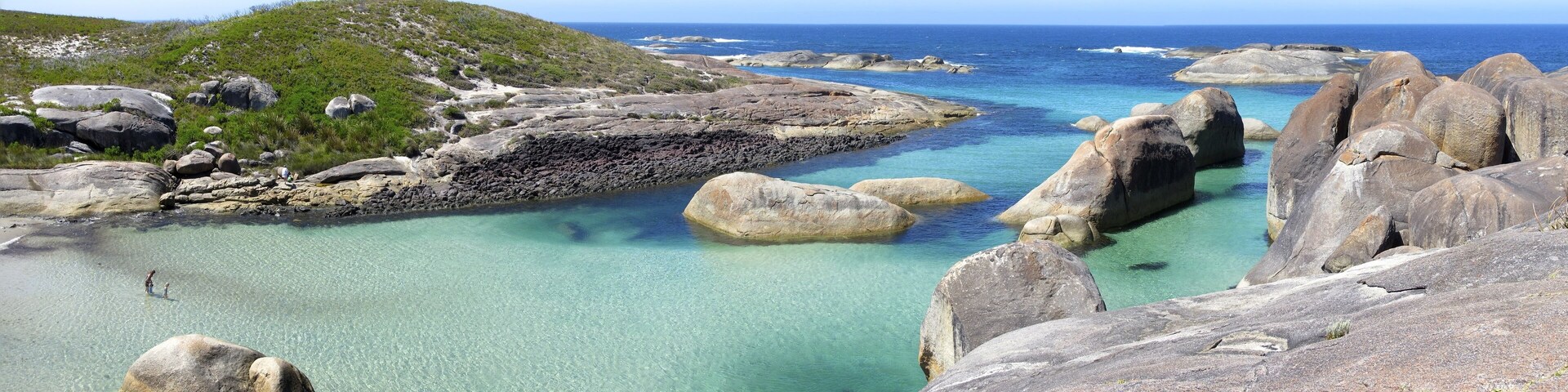 Un paisaje costero con aguas turquesas cristalinas, grandes rocas y una colina cubierta de hierba.