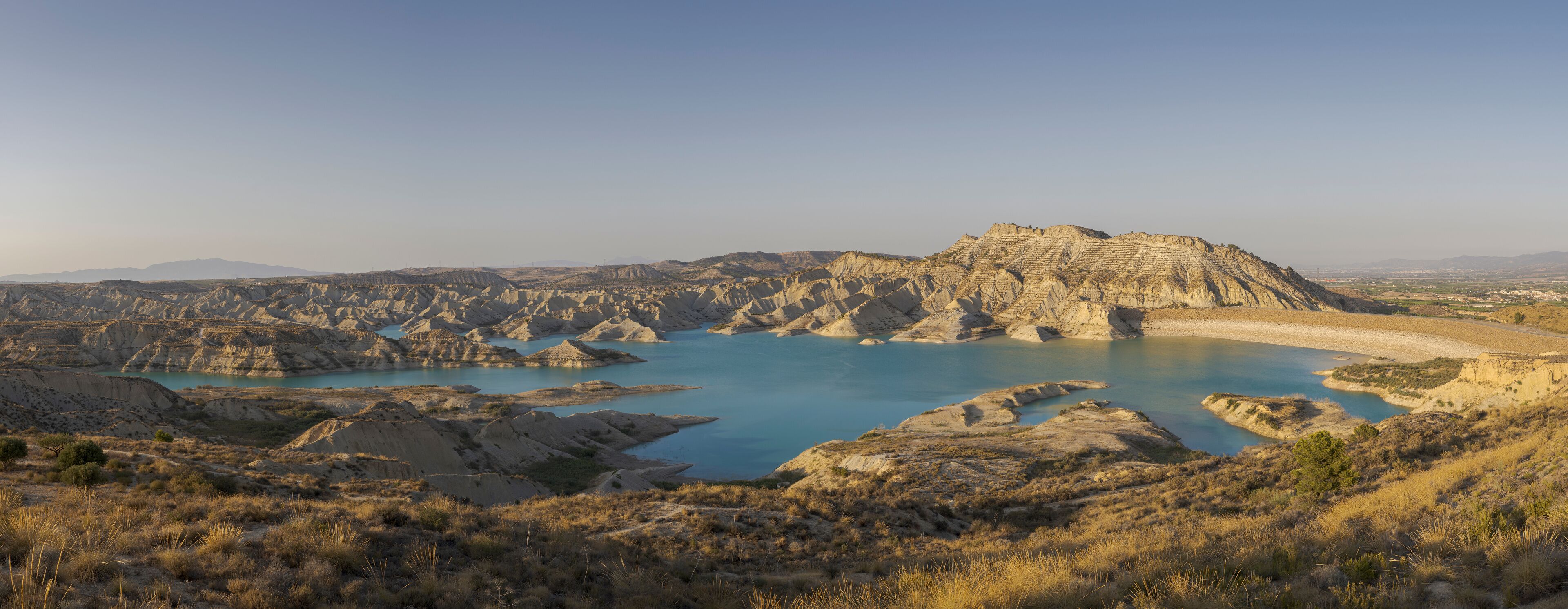 A rugged landscape with a large body of water surrounded by rocky terrain and sparse vegetation.