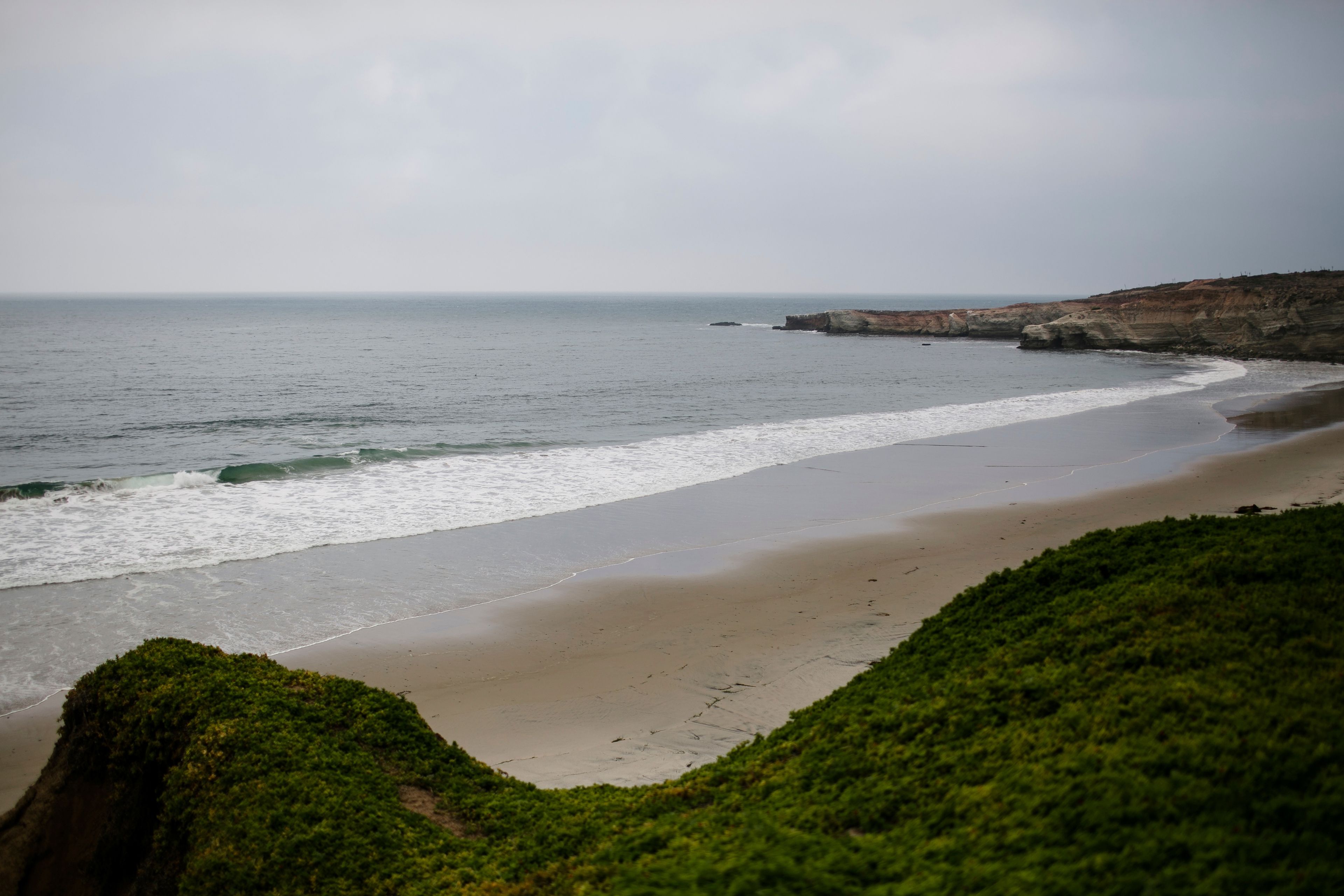 A coastal landscape with a sandy beach, gentle waves, and a cliff with vegetation.