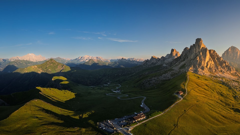 A mountainous landscape with a winding road, green valleys, and distant peaks.
