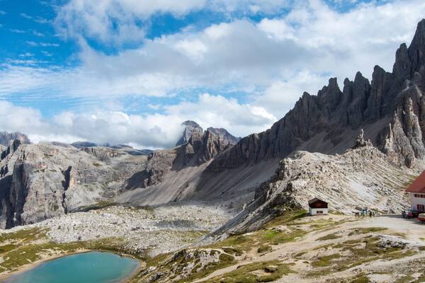 Paesaggio montano con una vetta imponente, un piccolo edificio con tetto rosso e un lago turchese.