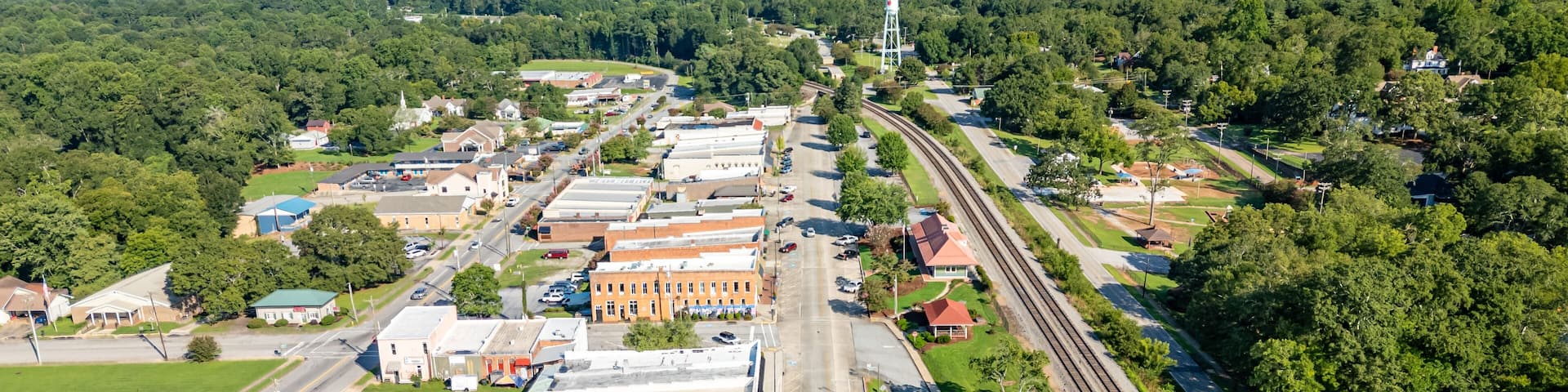 An aerial view of a town with a railway track, buildings, and green landscapes.