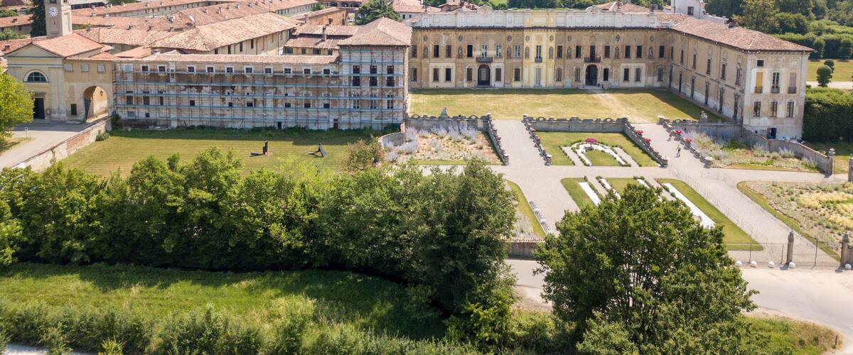 An expansive historical building complex with a central courtyard, surrounded by lush greenery and trees.