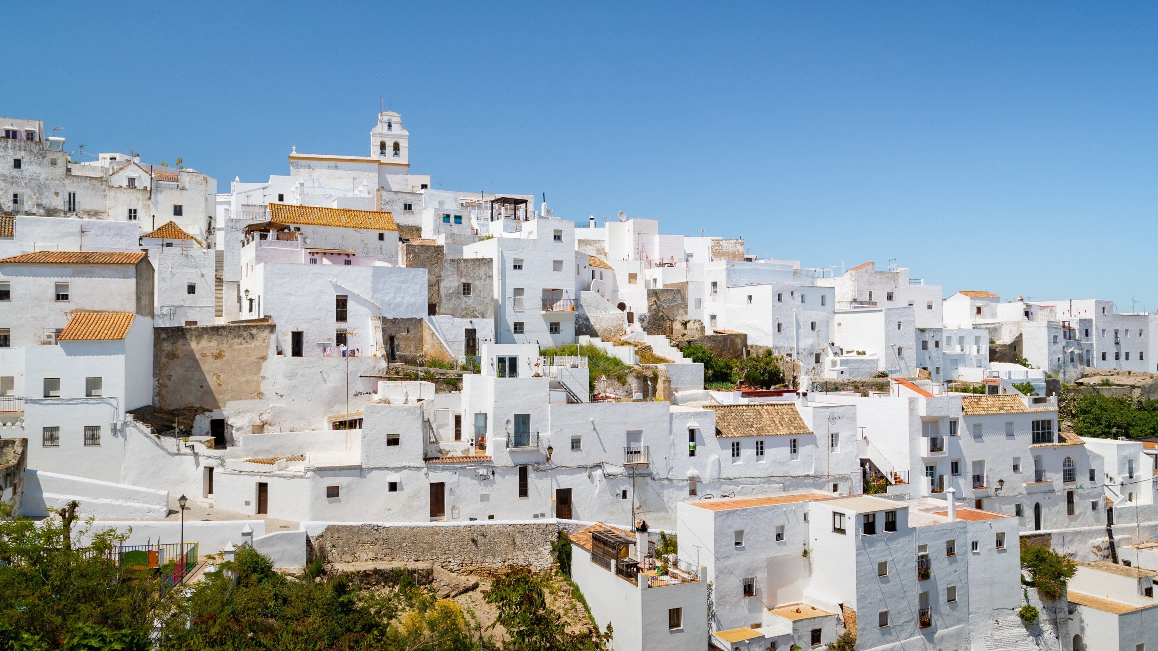 A white-washed hillside village with terracotta roofs and a prominent church tower.