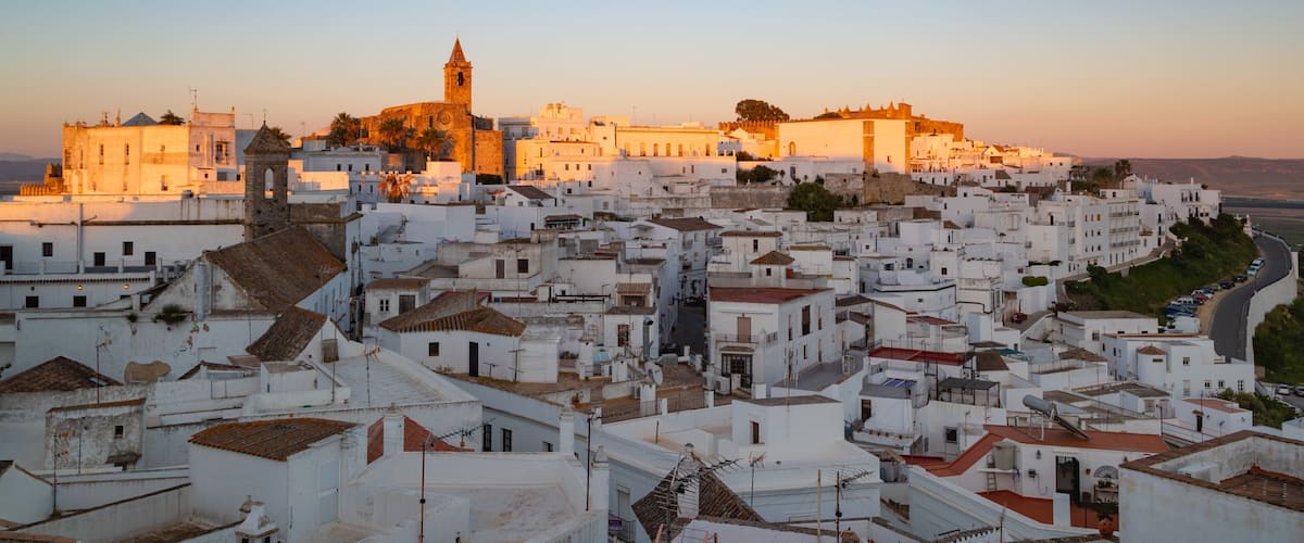 Une ville côtière aux bâtiments blancs, avec une église imposante et un château fortifié.