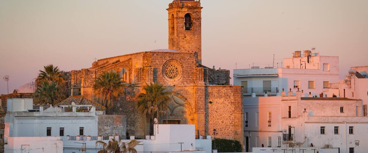 A historic church with a bell tower, palm trees, and white buildings.