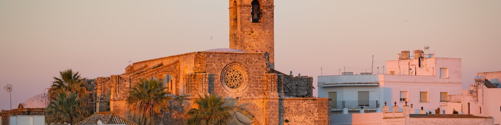 A historic church with a bell tower, palm trees, and white buildings.