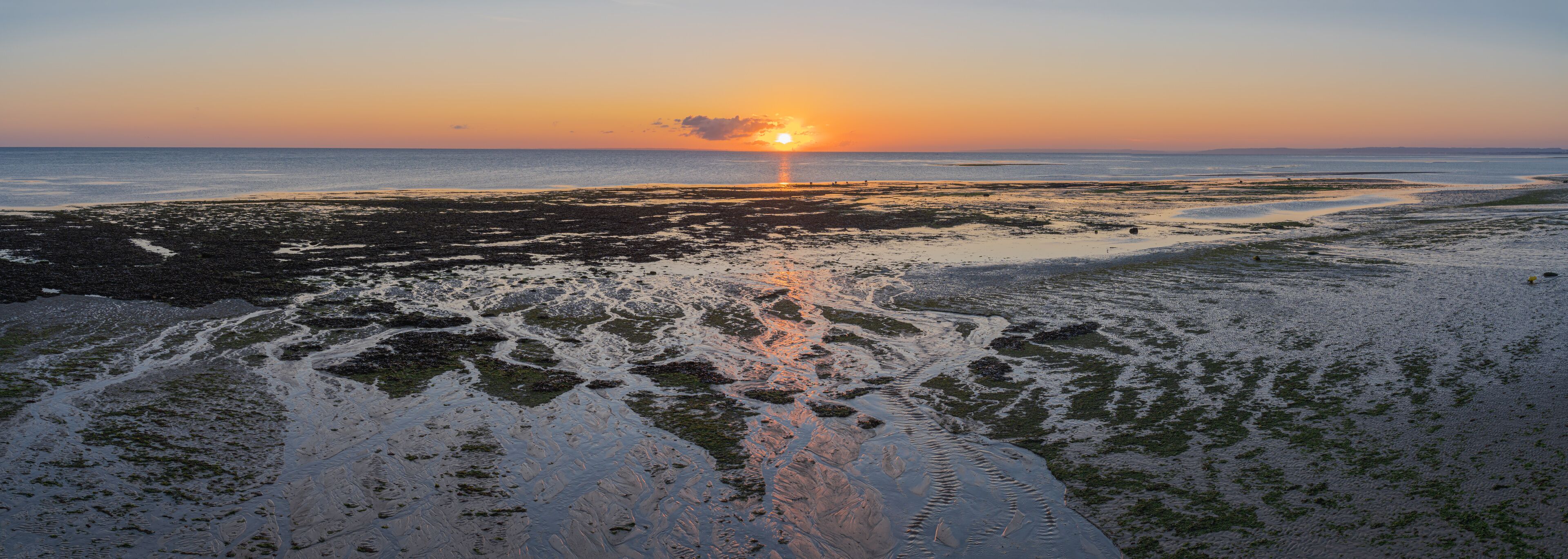 A sunset over a rocky beach with water reflecting the sky.