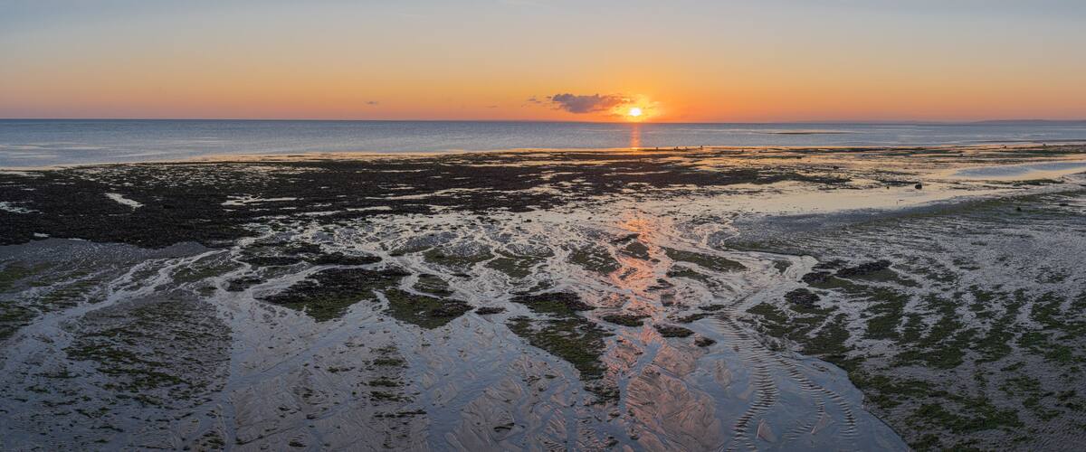 A sunset over a rocky beach with water reflecting the sky.