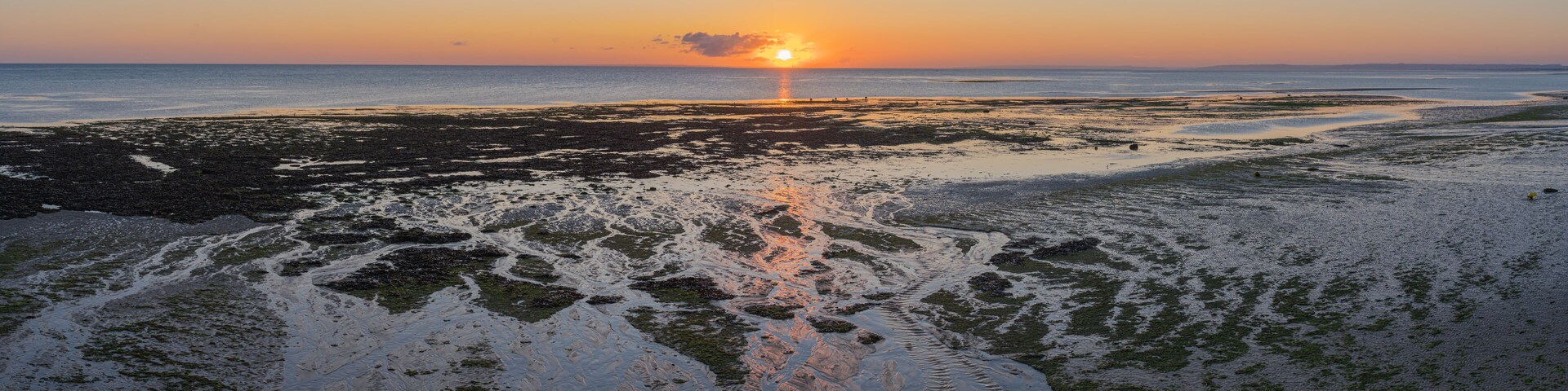 A sunset over a rocky beach with water reflecting the sky.