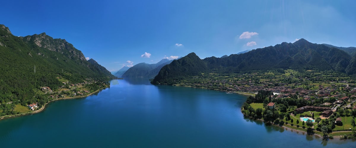 A lake surrounded by mountains, a small town, and a clear sky.