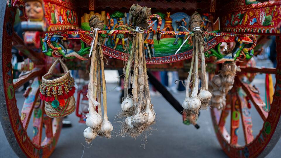 A colorful, intricately decorated cart with hanging bunches of garlic.