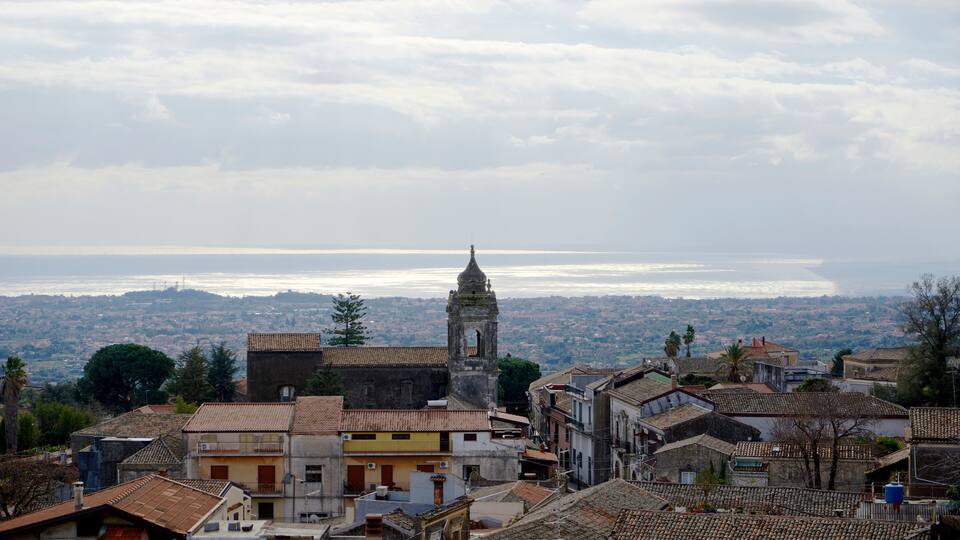 A coastal town with a prominent tower, terracotta-roofed buildings, and a view of the sea.