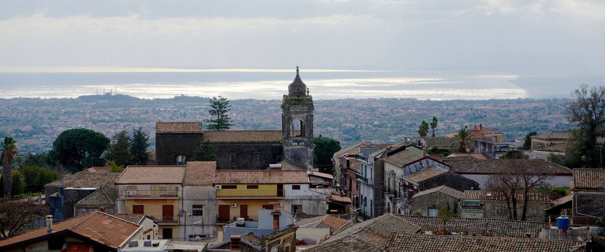 A coastal town with a prominent tower, terracotta-roofed buildings, and a view of the sea.
