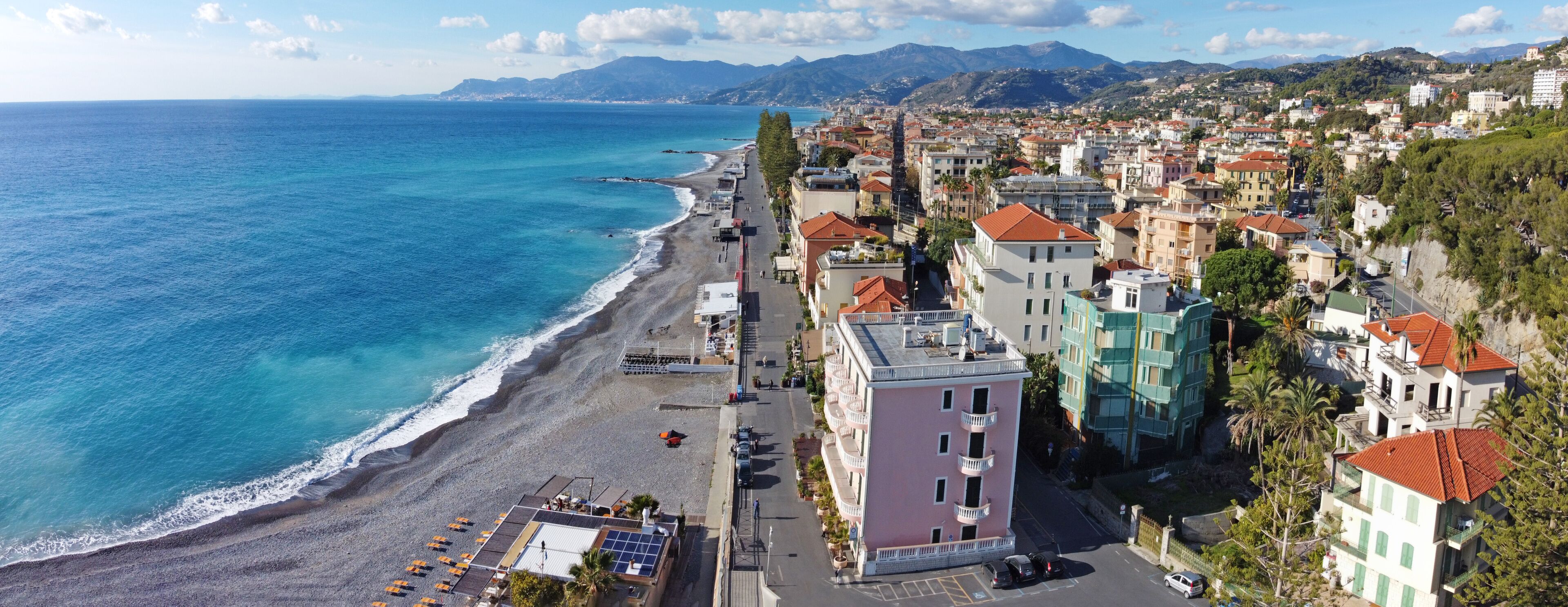 A coastal town with a beach, buildings, and mountains in the background.